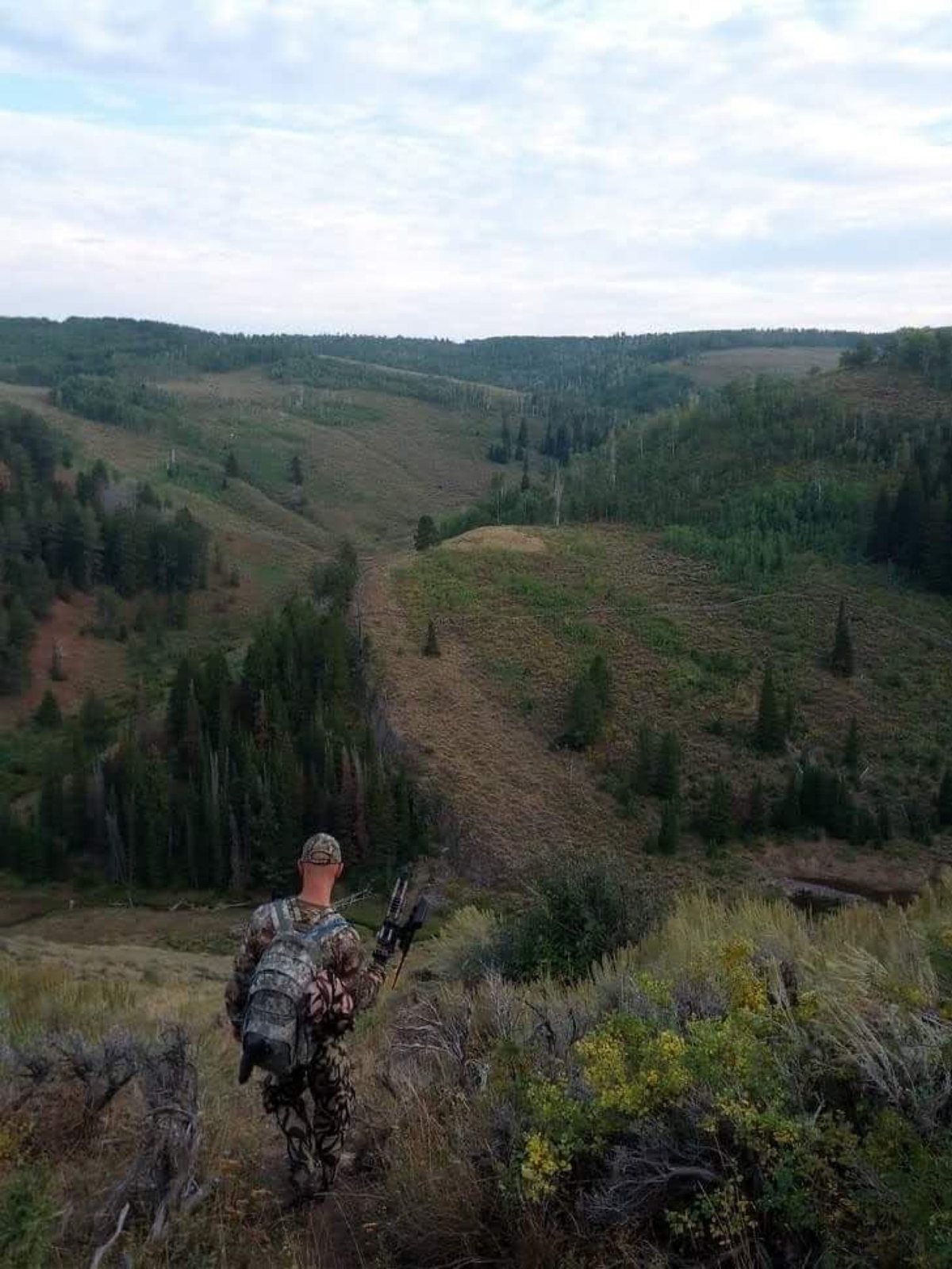 A bowhunter walking down a ridge toward a valley
